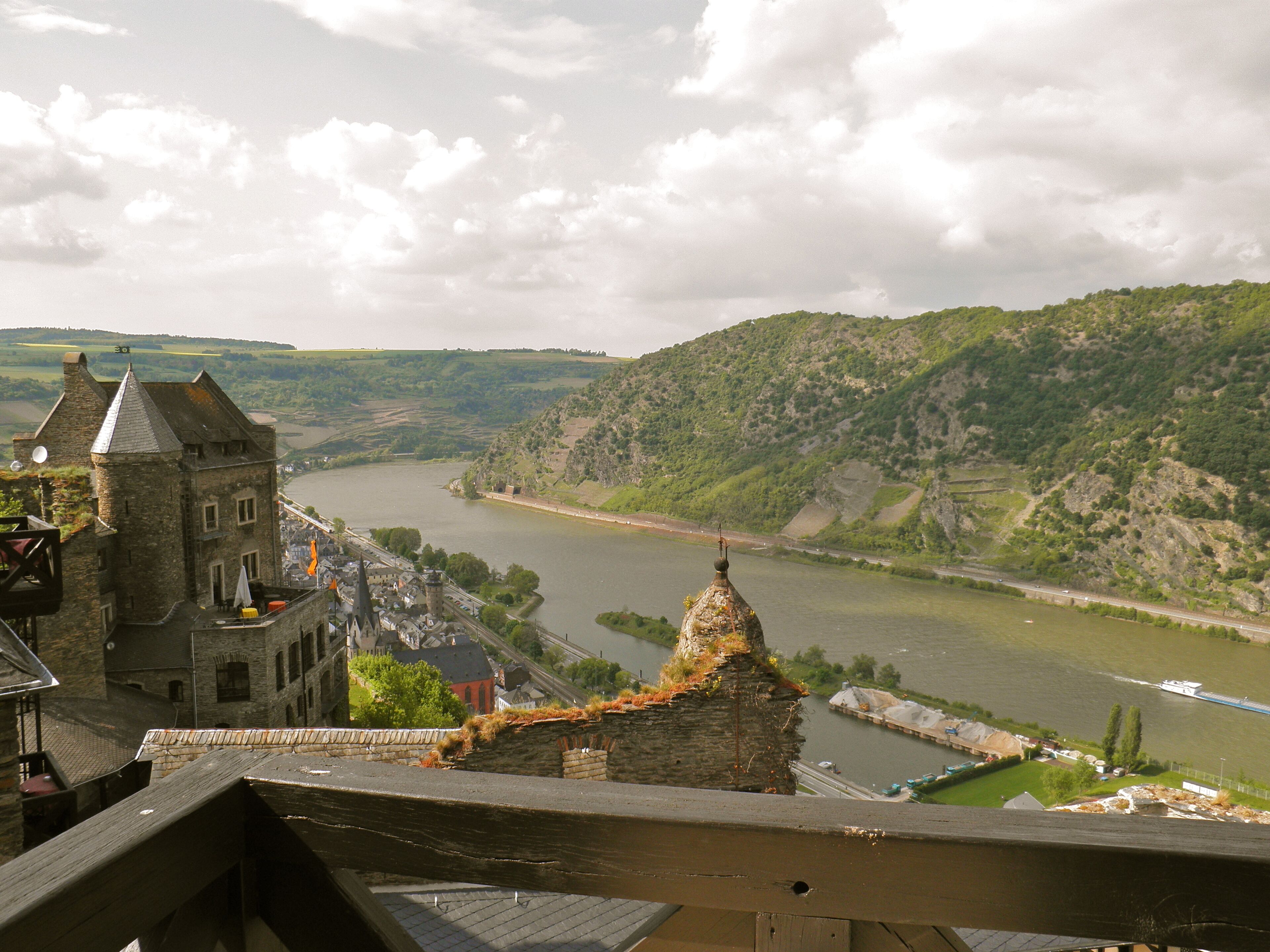 A historic building with a tower, overlooking a river and lush green hills.
