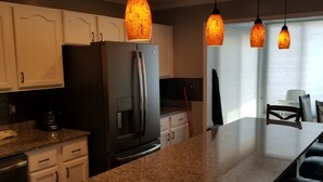 Een keuken met granieten aanrechtbladen, witte kasten, een roestvrijstalen koelkast en hangende lampen.