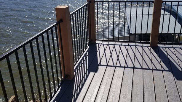 Een houten terras met een metalen hekwerk met uitzicht op een wateroppervlak.