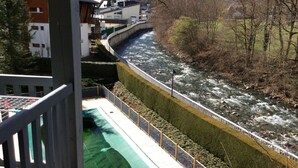 A view of a river with a bridge, buildings, and a fenced area with a green surface. - Beautiful apartment with mountain views (Saint-Lary-Soulan)