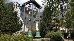 A bell tower with multiple bells, surrounded by lush greenery and a building in the background. - Beautiful apartment with mountain views (Saint-Lary-Soulan)