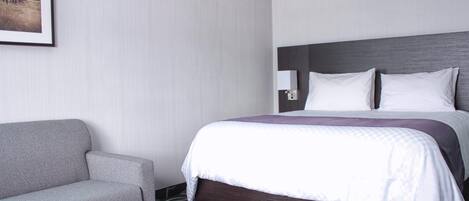 Una habitación de hotel con una cama, un sofá gris y un cuadro en la pared.