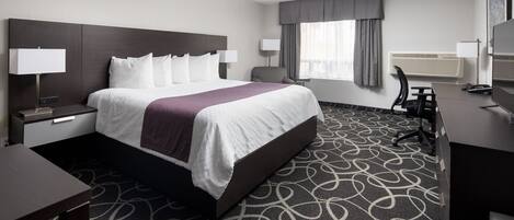 Habitación de hotel con una cama grande, dos mesitas de noche con lámparas, un escritorio con silla, un televisor y una ventana con cortinas.