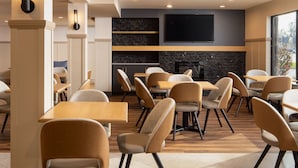 A modern restaurant interior with wooden tables and chairs, a stone wall, and a flat-screen TV mounted above the seating area.
