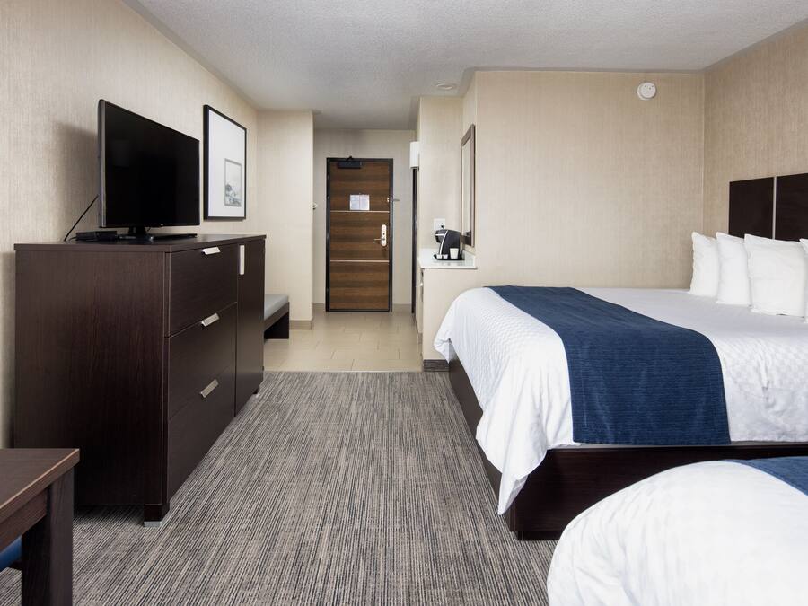 Ein Hotelzimmer mit einem Bett, einem Fernseher auf einer Kommode, einem Schreibtisch und einer Tür zu einem Badezimmer.