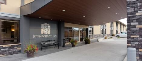 Exterior del Stonecroft Inn con un diseño moderno, que incluye un paseo techado, un banco y plantas en macetas.