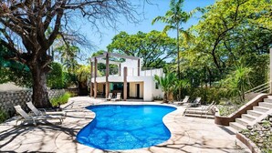 A modern house with a swimming pool, surrounded by lush greenery and a stone wall.