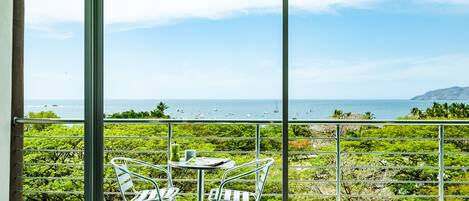 Un balcón con mesa y sillas, con vistas a un paisaje marino y vegetación.