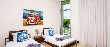 Een hotelkamer met twee bedden, een schilderij van een busje, een balkon met gordijnen en een kamerbreed tapijt met een patroon.