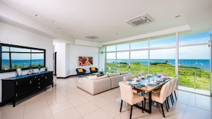 A modern living room with a dining area, large windows with a view of the sea, and a black entertainment unit.