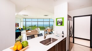 A modern kitchen with a large window, a stainless steel refrigerator, and a fruit bowl on the counter.