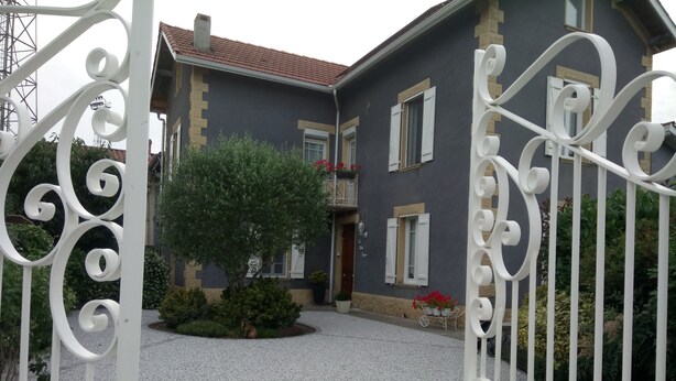 Ein zweistöckiges Haus mit einem Schotterweg, einem Baum und einem weißen Metalltor.