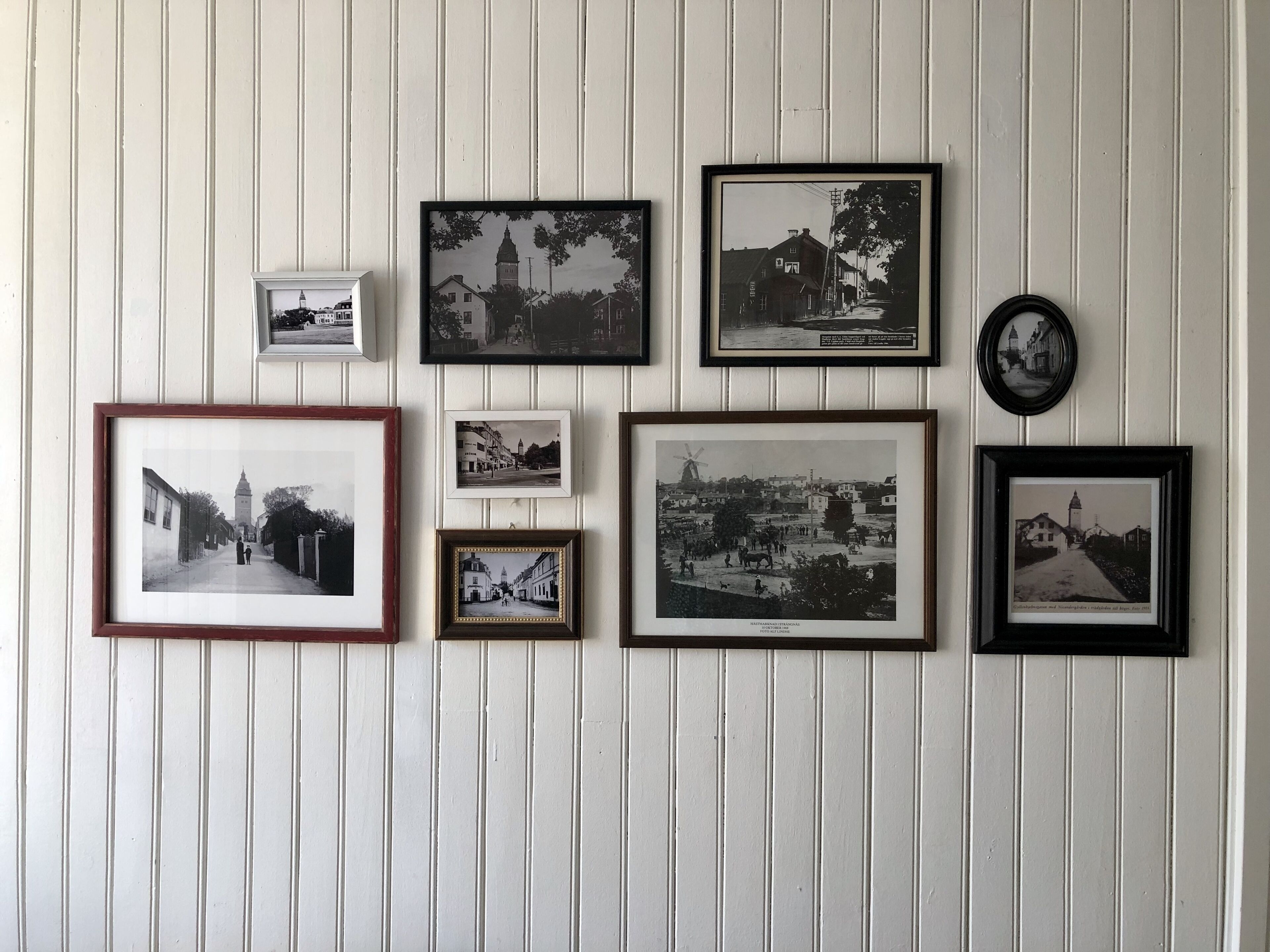 Un mur orné de plusieurs photographies en noir et blanc, encadrées, représentant différents bâtiments et rues.