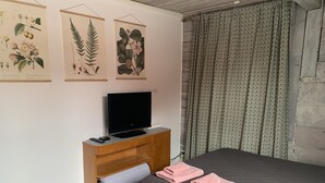 Ein Schlafzimmer mit einem Bett, einem Fernseher auf einer Holzablage und botanischen Drucken an der Wand.