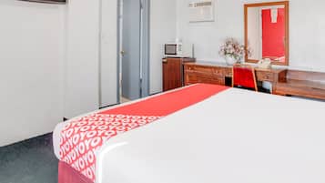 A hotel room with a bed, a desk, a chair, a dresser, a mirror, a microwave, and a door.