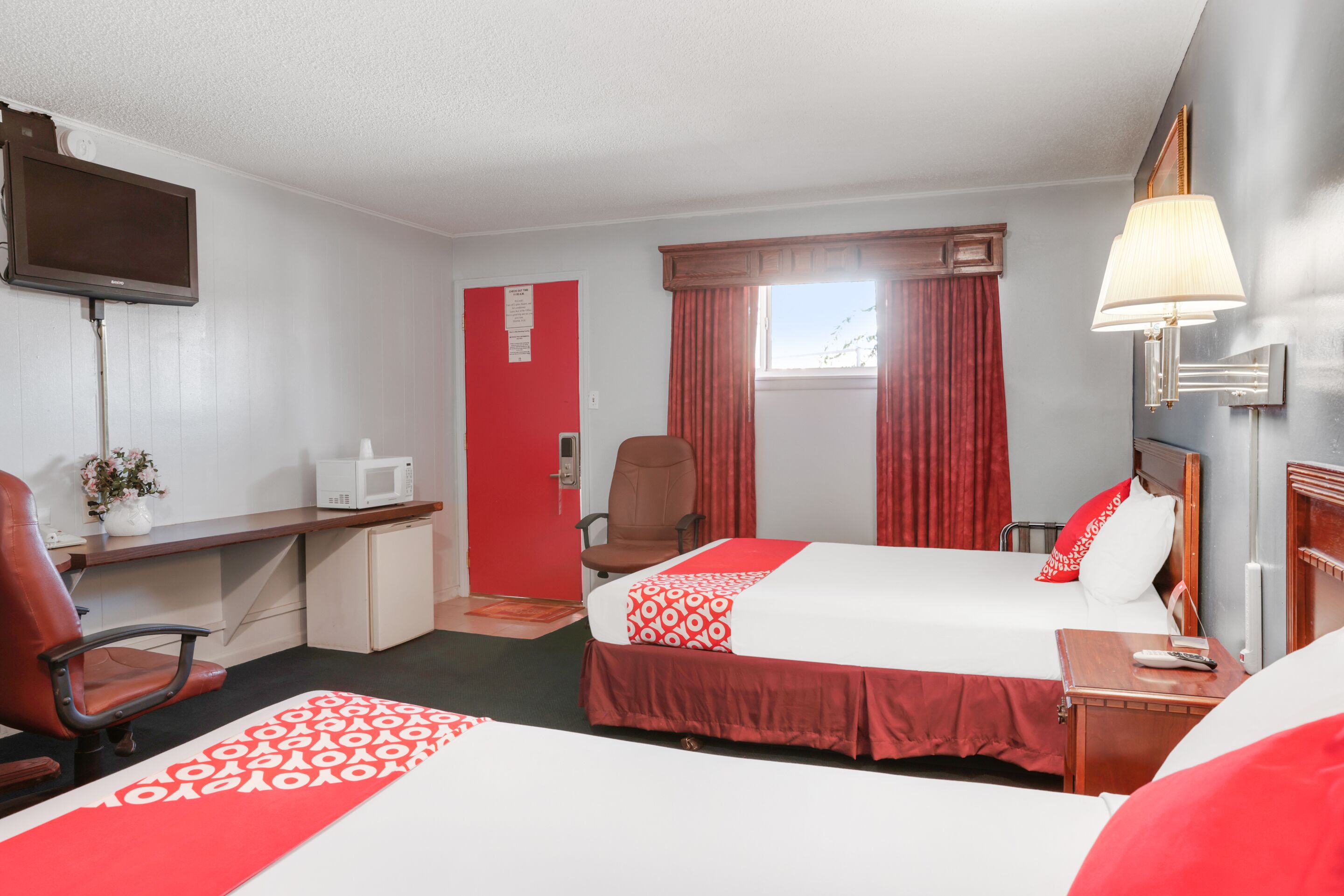 A hotel room with two beds, a desk with a computer, a chair, a TV, and a window with curtains.