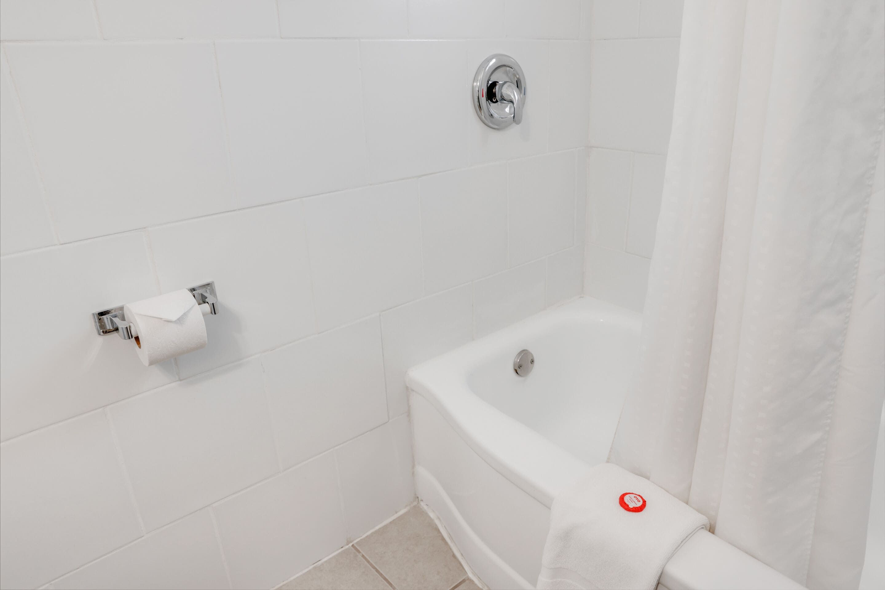 A bathroom with white tiles, a bathtub, a toilet paper holder, and a shower curtain.