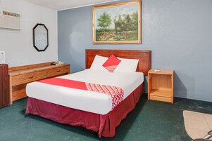 Habitación de hotel con una cama grande, cabecera de madera, una mesita de noche, un tocador y un cuadro en la pared.