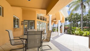 An outdoor patio with a table and chairs, surrounded by a yellow wall and palm trees. - Sunny Retreat by VillaDirect (Davenport)
