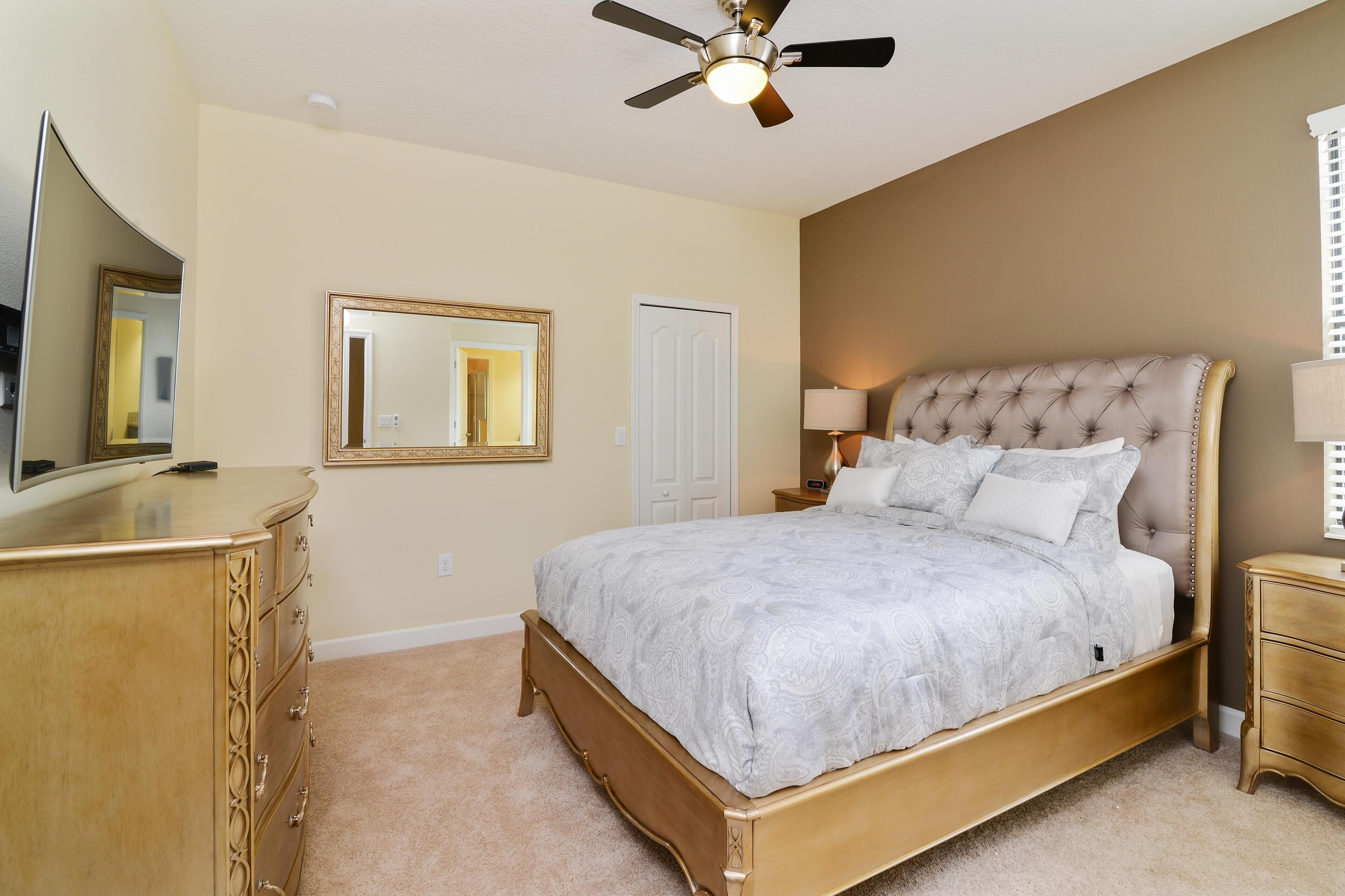 A bedroom with a bed, dresser, ceiling fan, and a mirror.