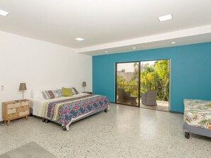 Quarto com cama, mesa de cabeceira, cadeira e varanda com vista para vegetação.