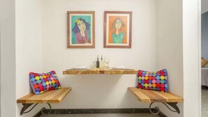 A room with two wooden benches, colorful polka dot cushions, a small table with a glass, and two framed artworks on the wall. - Casa Orozco (Cali)