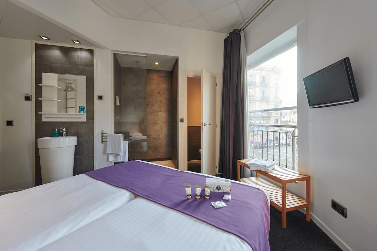 A hotel room with a bed, a bathroom, a TV, and a balcony.