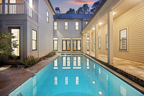 Una piscina rectangular con borde de azulejos, rodeada por un patio con baldosas de piedra y una planta pequeña.