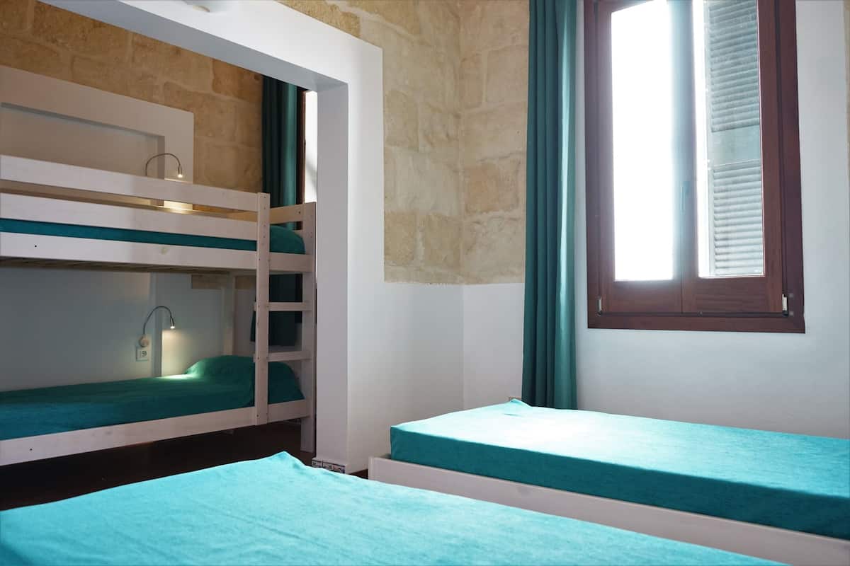 Ein Zimmer mit Etagenbetten, einem Fenster mit Jalousien und einer Steinwand.
