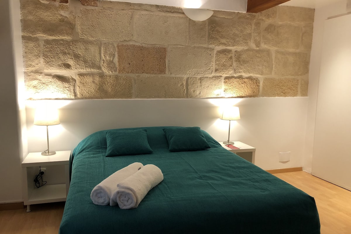 Ein Zimmer mit einer Steinsäule, einem grünen Bett mit zwei Kissen, zwei Nachttischlampen und einem zusammengerollten Handtuch auf dem Bett.
