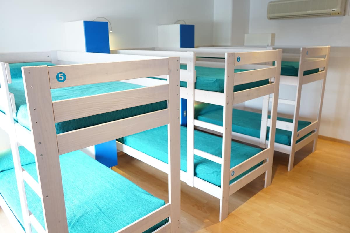 Zwei Etagenbetten mit blaustichigem Bettzeug und Holzrahmen, in einem Zimmer mit Holzboden und weißen Wänden.