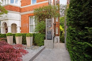 A red brick building with white trim, a gated entrance, and a pathway leading to a door marked 'FLAT 1.'