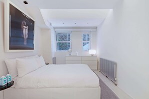 A bedroom with a bed, a dresser, a vanity with a mirror, and a radiator.