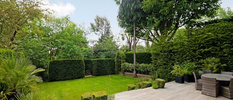 A wooden deck with outdoor furniture, a well-maintained lawn, and various shrubs and trees.