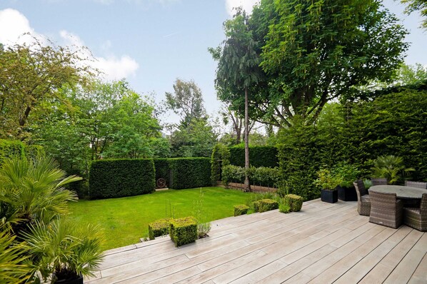 A wooden deck with outdoor furniture, a well-maintained lawn, and various shrubs and trees.