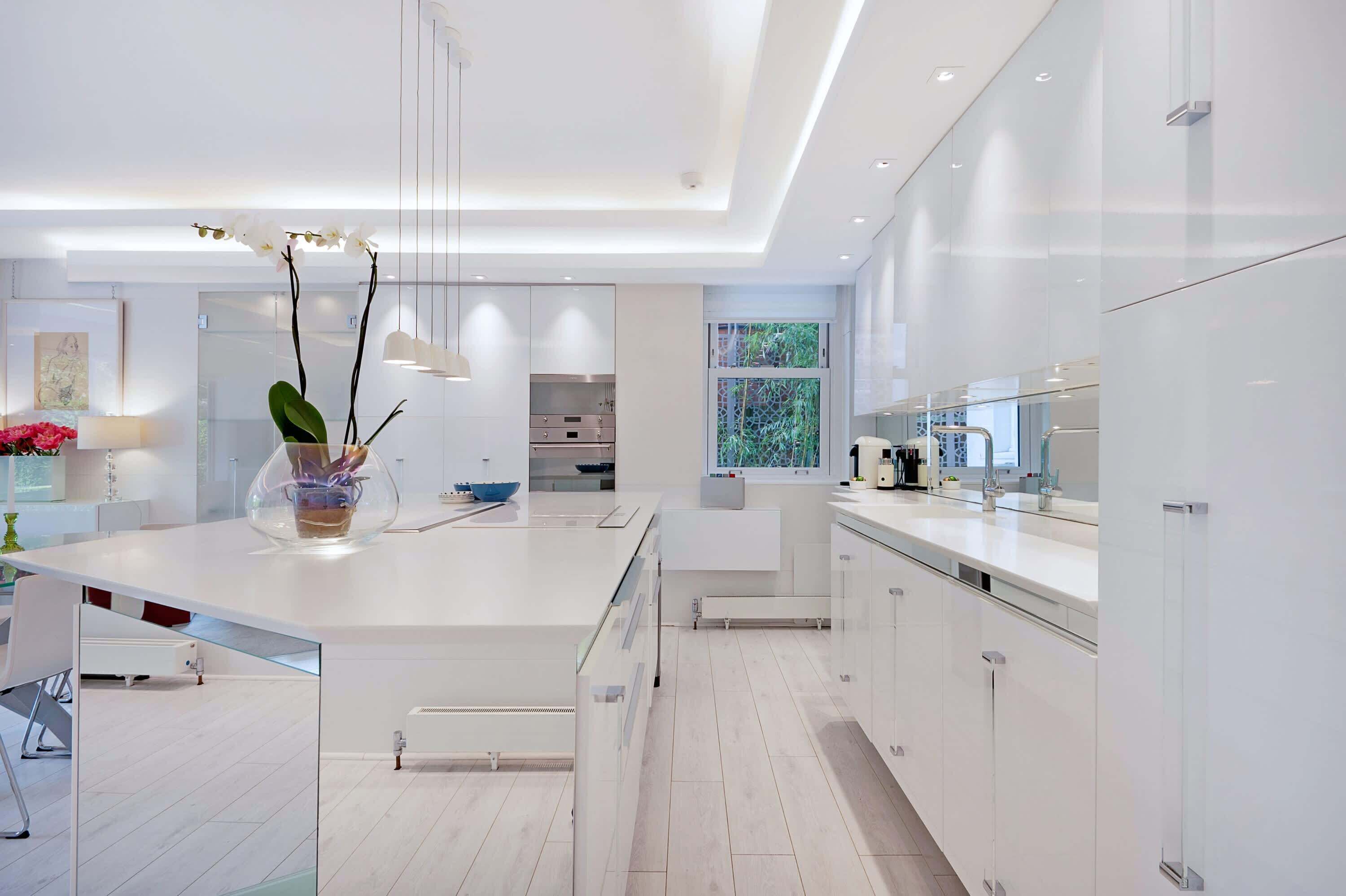 A modern kitchen with white cabinetry, a central island, and a view of greenery outside.