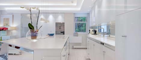 A modern kitchen with white cabinetry, a central island, and a view of greenery outside.