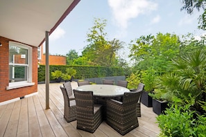 An outdoor patio with a round table and wicker chairs, surrounded by greenery and a brick wall. - The White Peace Garden 3 bed Hampstead - by Out of Office Lifestyle (London)