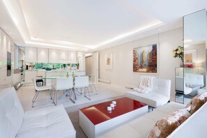 A modern living room with a glass dining table, white sofas, and a red coffee table.