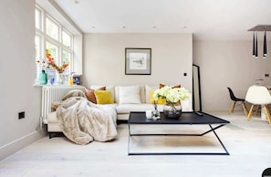 A modern living room with a sofa, a coffee table, and a window with flowers. - The English Gentleman, Hampstead Heath - by Out of Office Lifestyle (London)