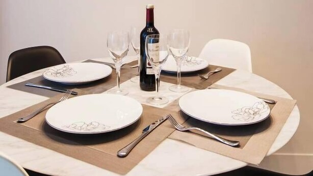 Una mesa de comedor dispuesta con platos, cubiertos y copas de vino, junto con una botella de vino y una de agua.