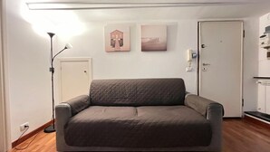 A room with a grey sofa, a floor lamp, and two wall-mounted artworks. - Casa Daniele (010025-LT-1249) (Genova)