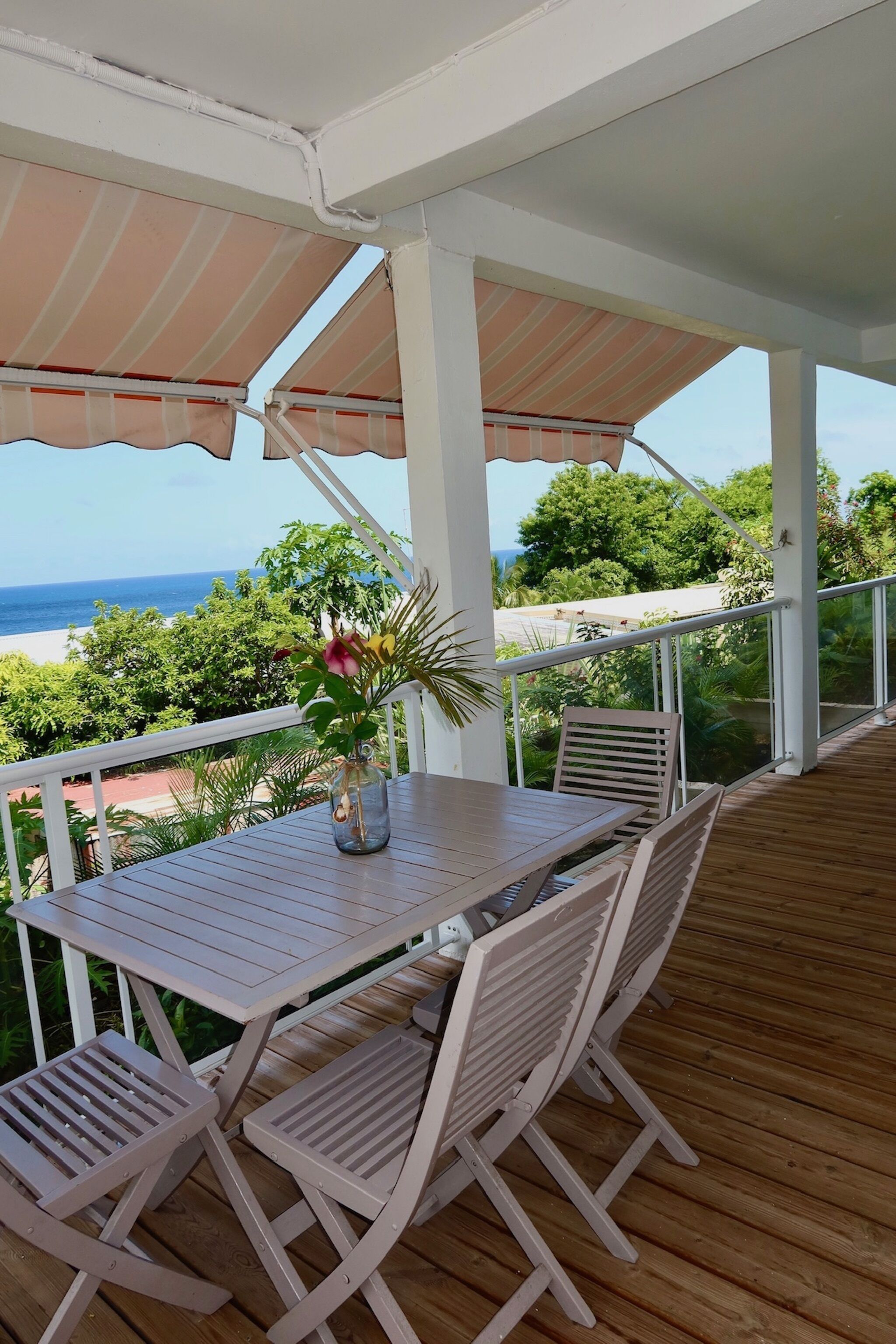 A covered outdoor seating area with a table and chairs, overlooking a beach.
