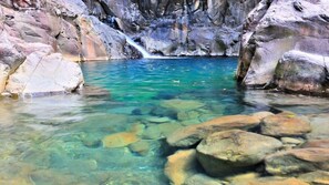 A clear pool surrounded by large rocks and a waterfall in the background.