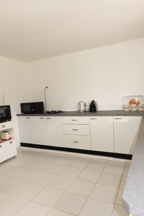 Une cuisine moderne avec des meubles blancs, un micro-ondes noir, une cuisinière à gaz et une machine à café.