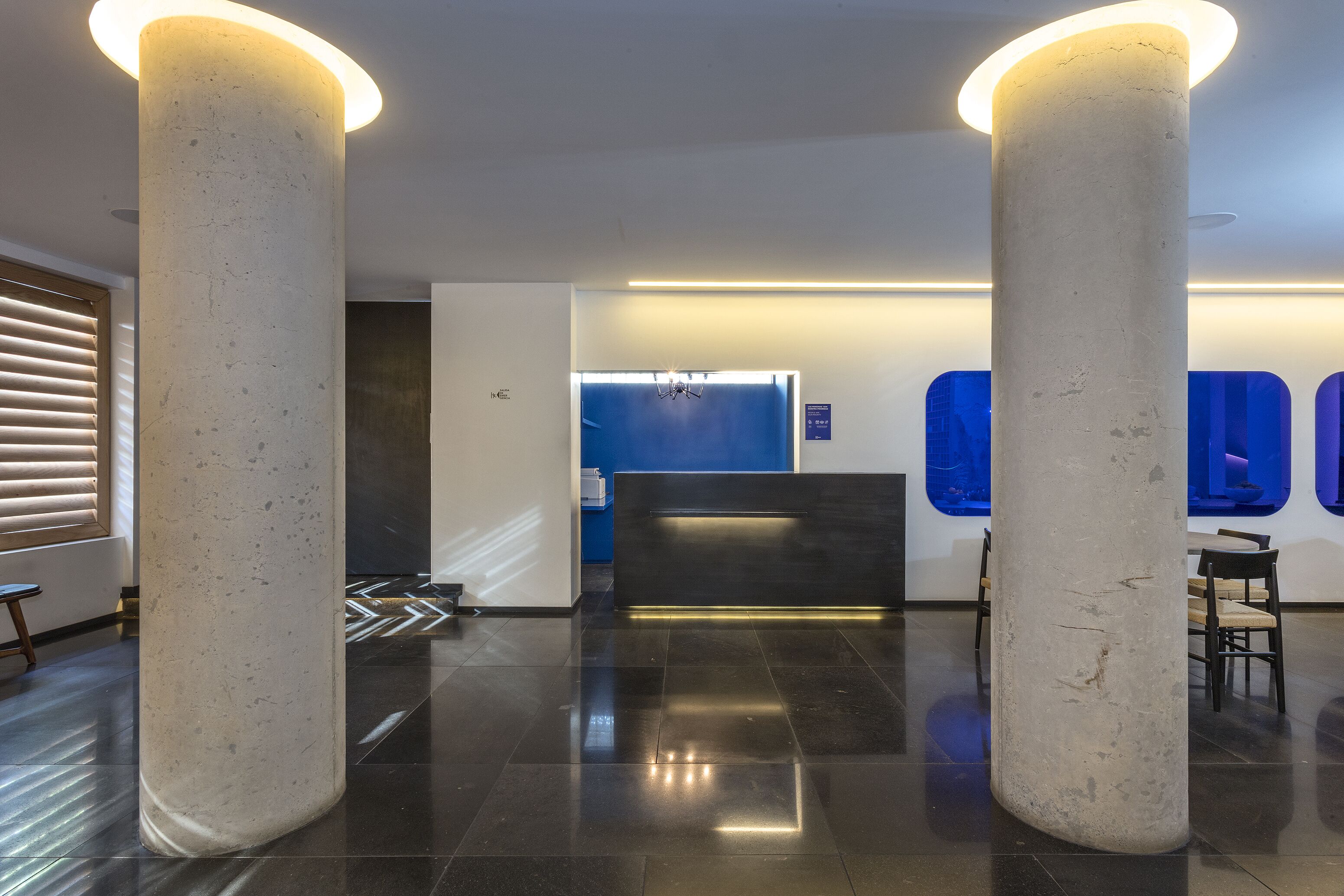 Un vestíbul modern amb dues columnes blanques grans, una taula de recepció i una paret blava amb finestres.