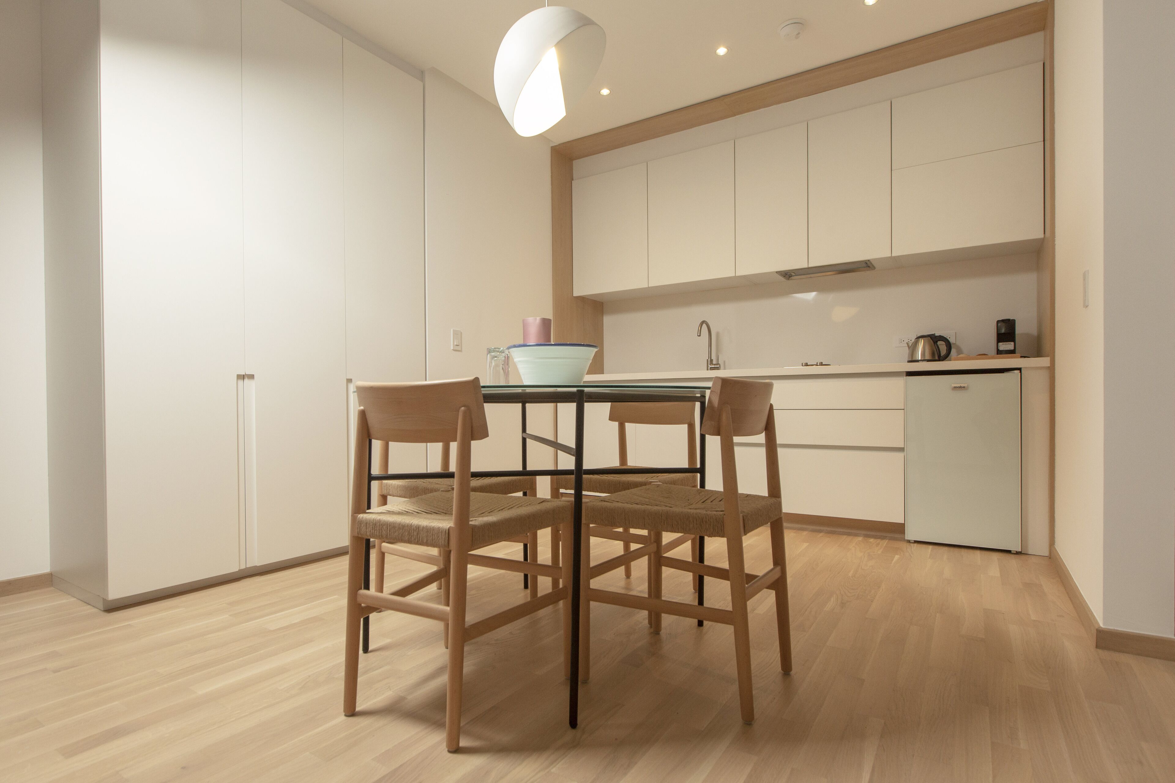 A modern kitchen with white cabinets, a wooden dining table with chairs, and a light-colored floor.