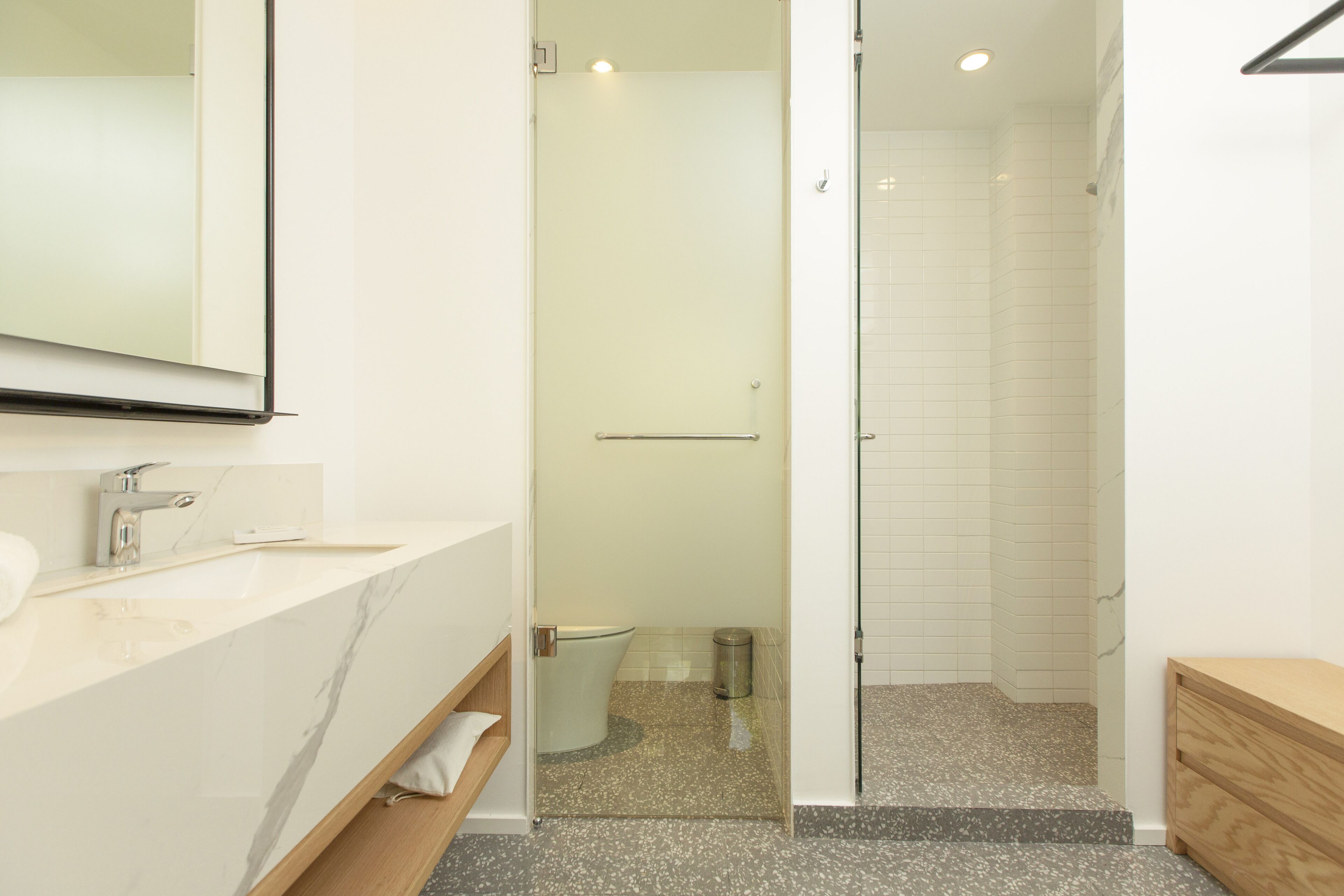 A modern bathroom with a marble sink, a glass shower enclosure, and a wooden vanity.
