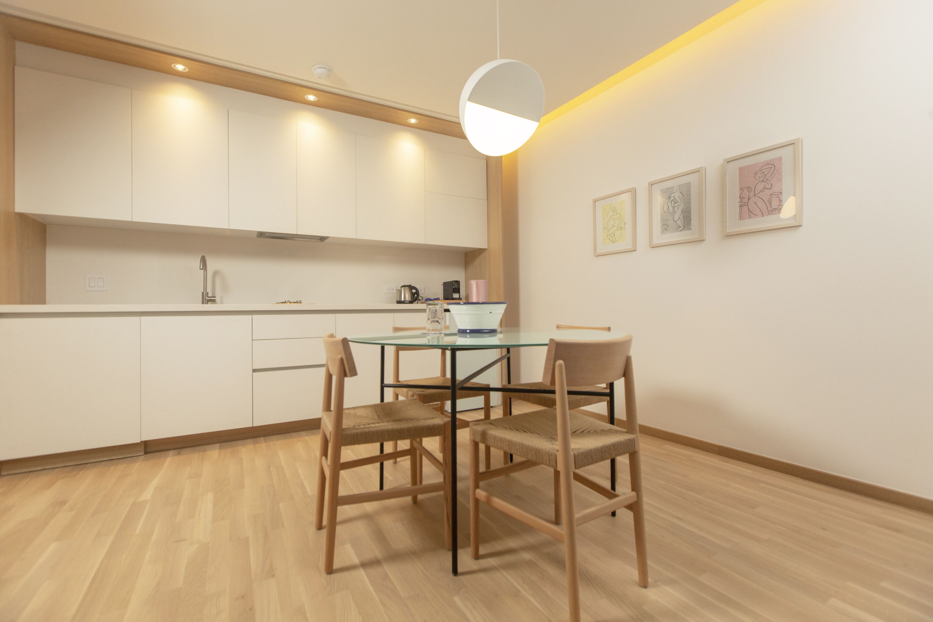 Une cuisine moderne avec une table ronde en verre, des chaises en bois et un luminaire suspendu.