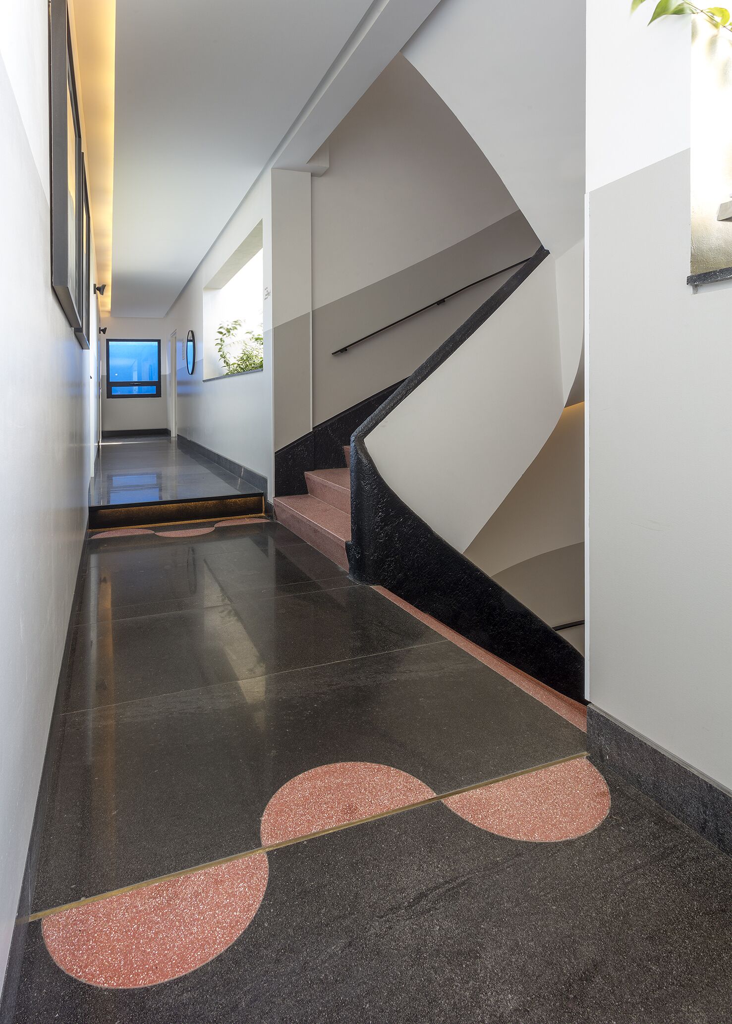 Een modern interieur met een gepolijste vloer, een trap met een zwarte leuning, en een hal die naar een kamer met een raam leidt.